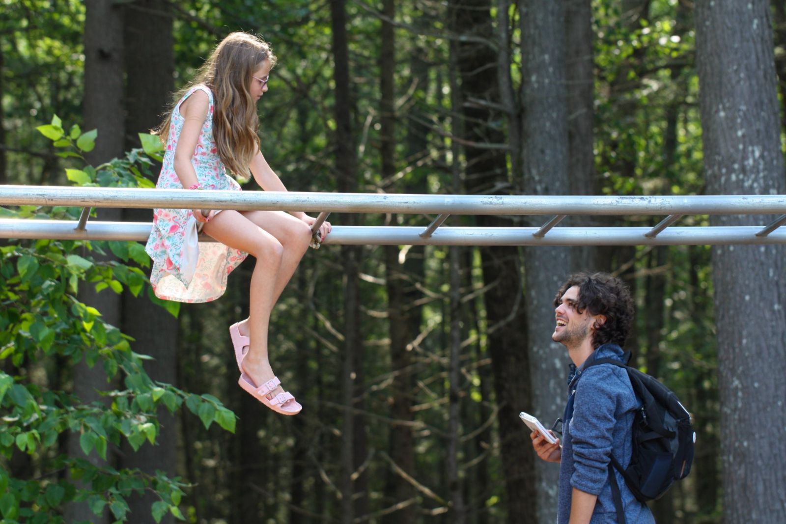 A student on an outdoor climbing structure talking with a smiling tutor in the summer woods
