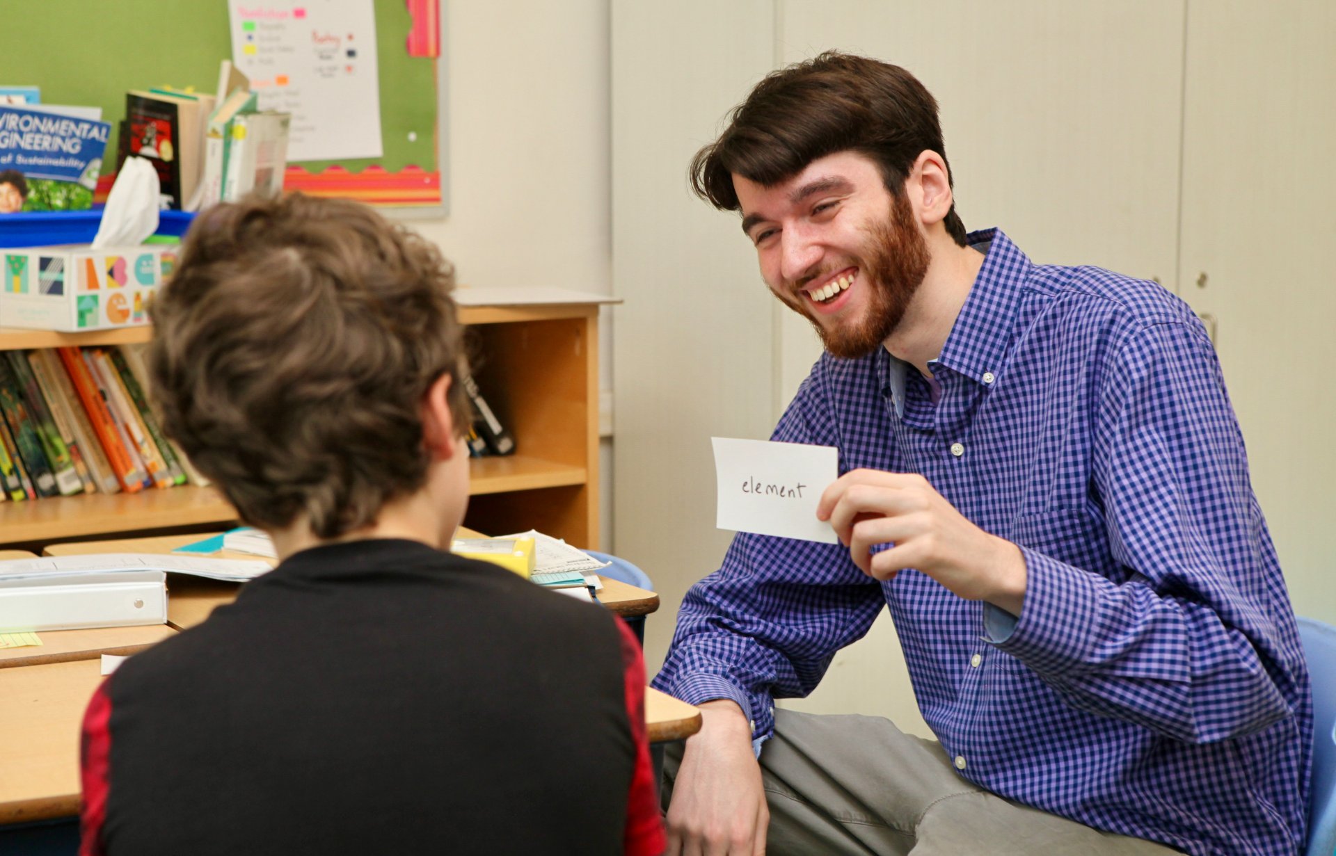 A tutor smiling and holding up a word card during a one-on-one reading lesson