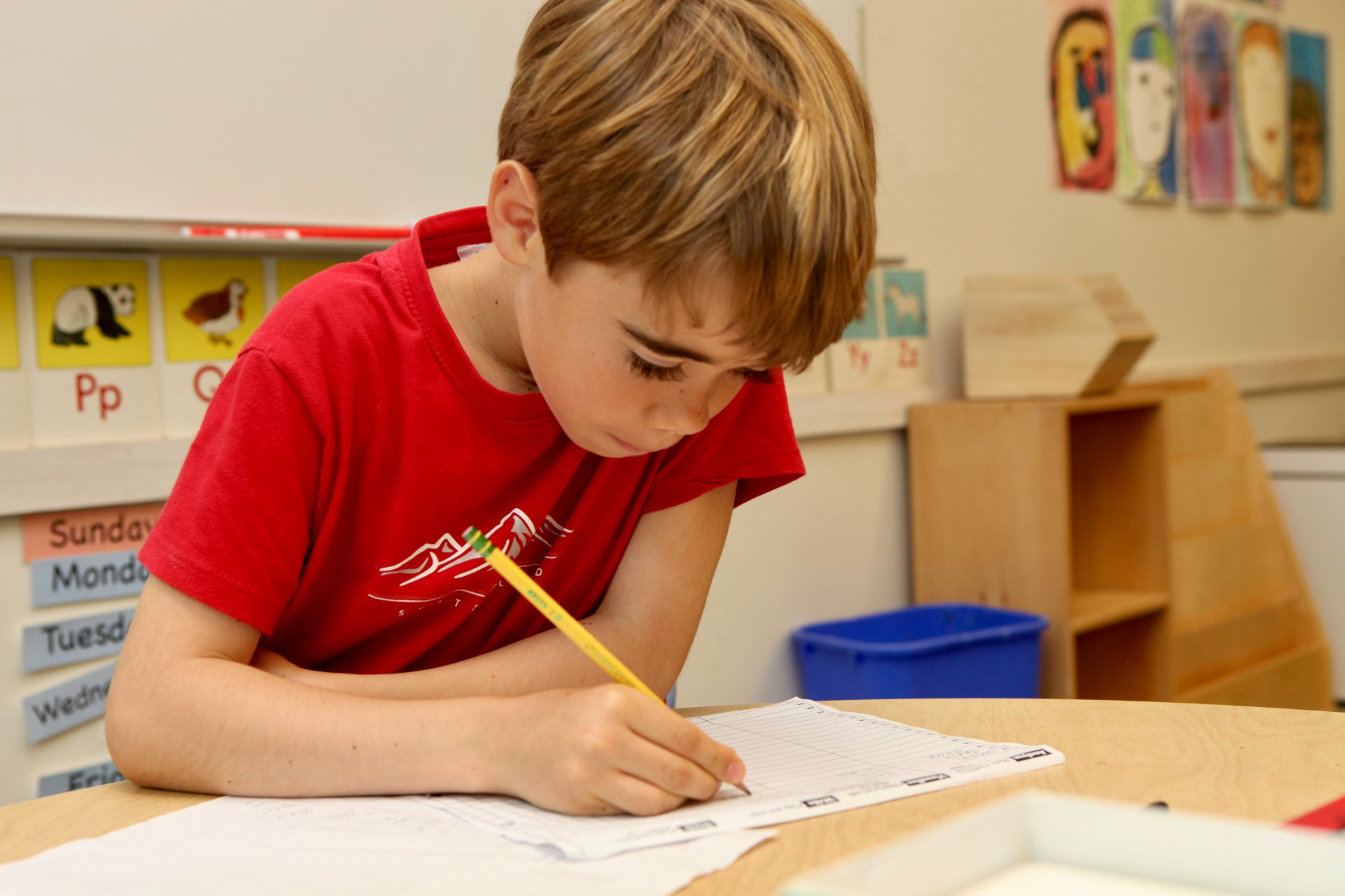 A student looking down, writing with a pencil at a classroom table
