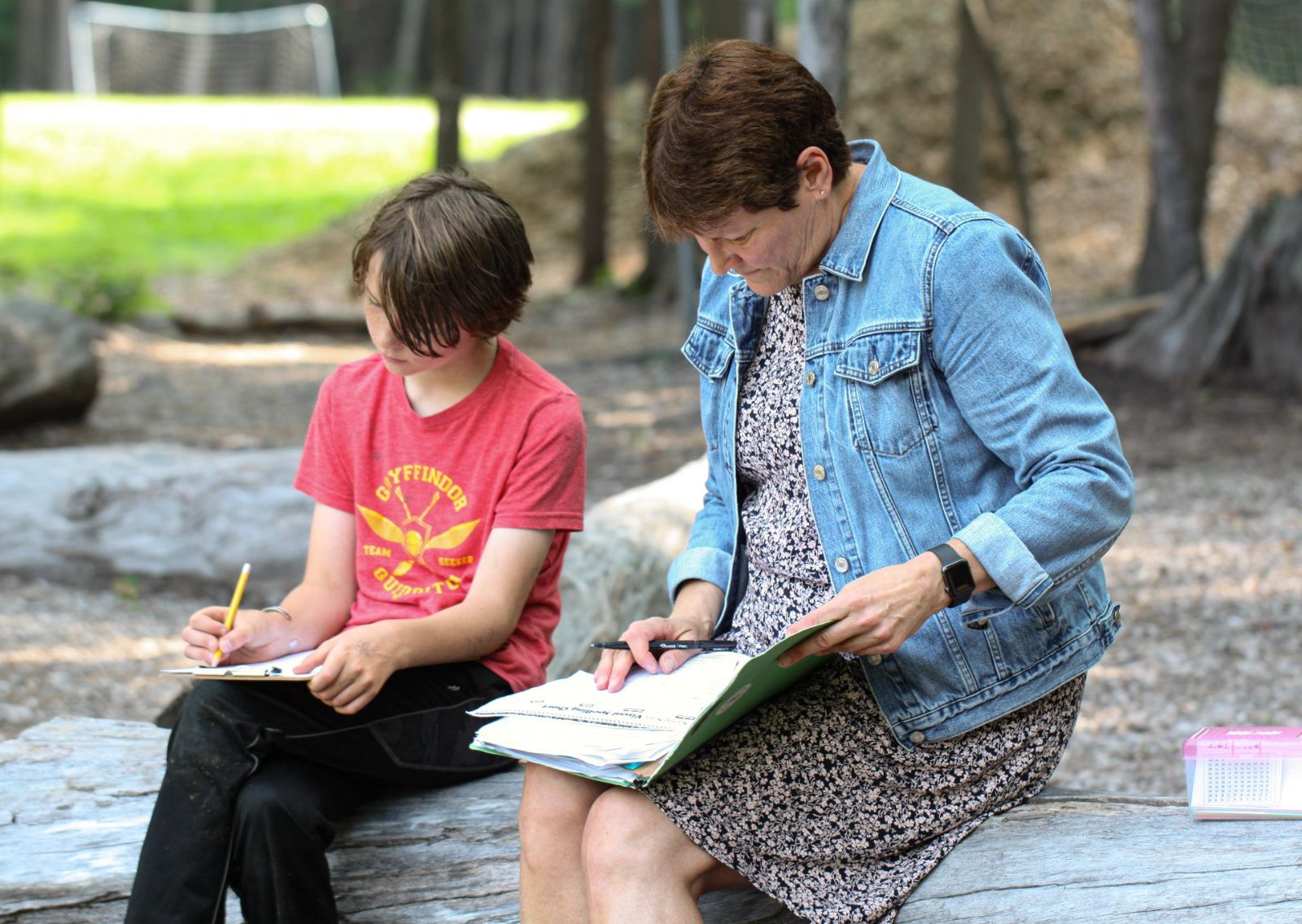 A tutor and student writing together at an outdoor table